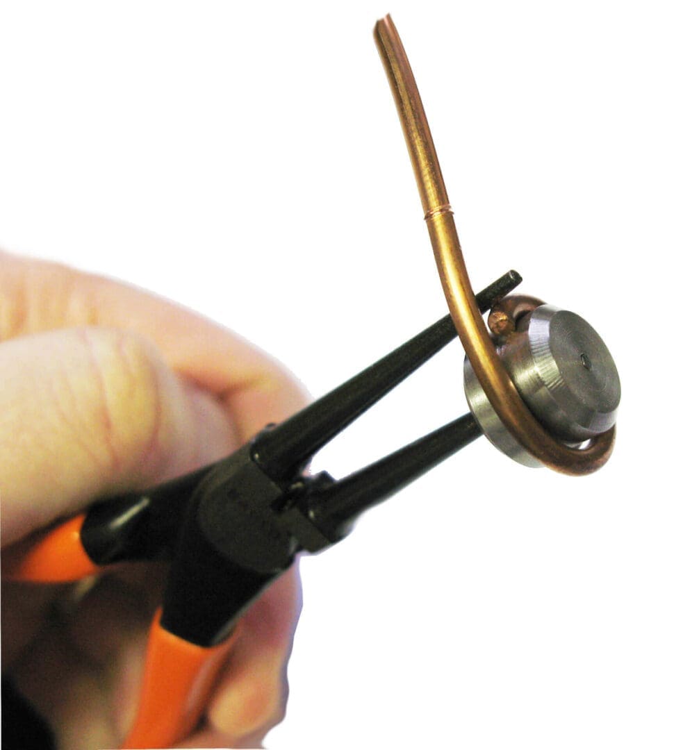 Pliers gripping copper-wrapped metal disc