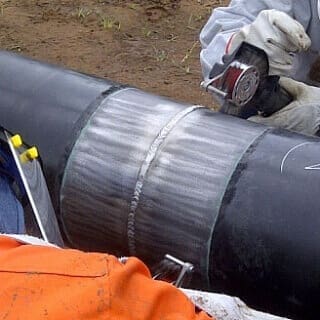 Worker grinding weld on steel pipeline