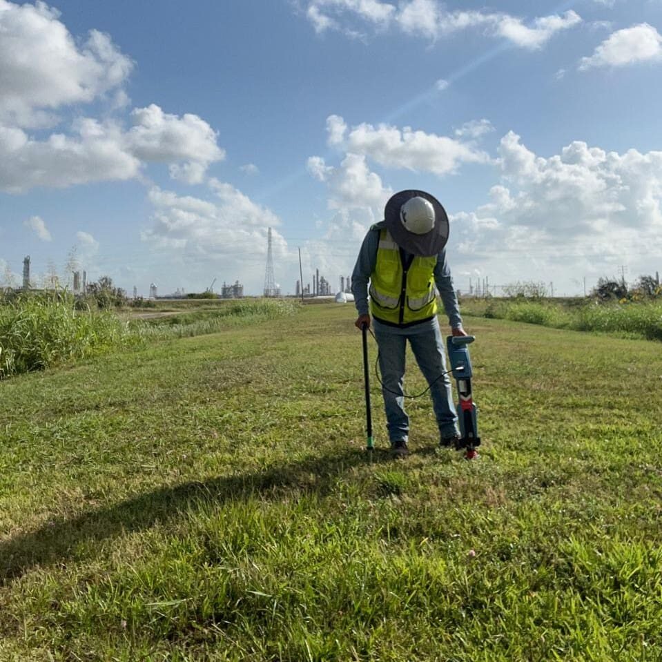 Surveyor with locator in grassy industrial field