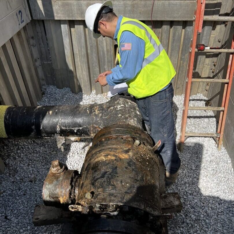 Worker in hardhat inspecting large rusted valve