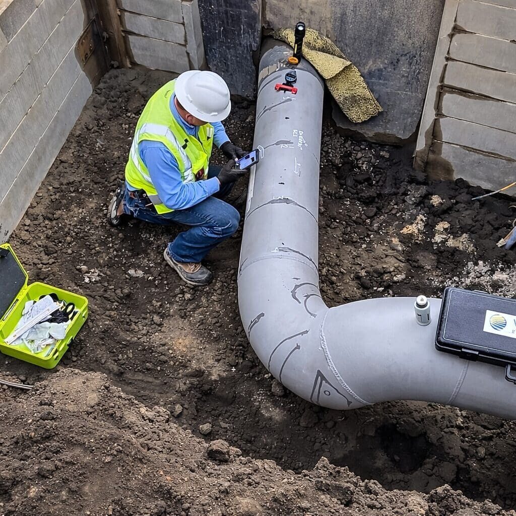Worker inspecting coated underground pipeline in trench