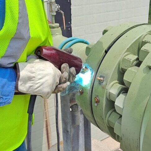 Industrial worker welding valve on green pipeline