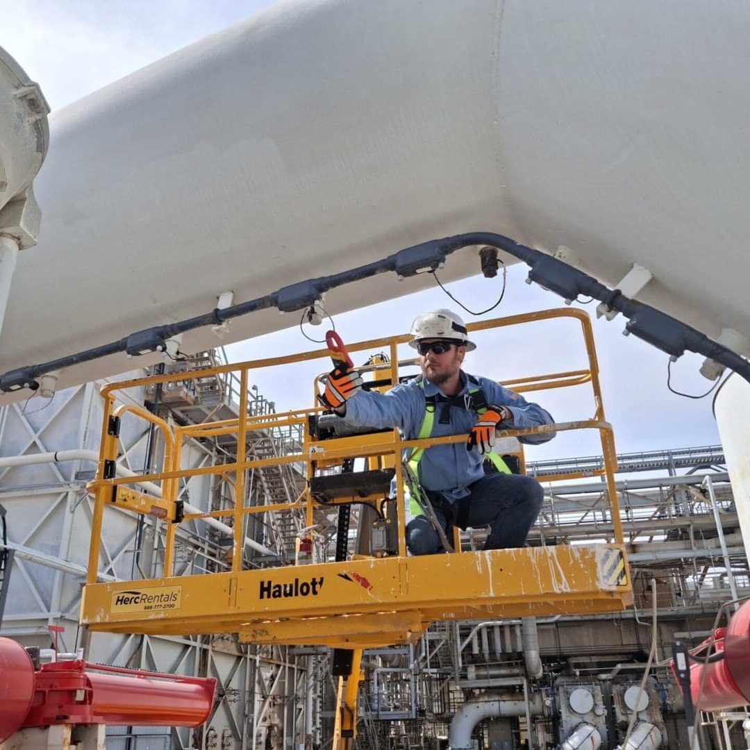 Construction worker on aerial lift inspecting industrial pipes